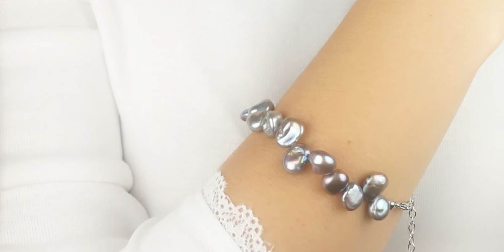 Stylowa bransoletka damska srebrna z perłami QUEEN na ręce Stylowa bransoletka damska srebrna z perłami ubrana na ręce. Bransoletka posiada przedłużkę na której końcu zawieszona jest zawieszka z logo Rosett