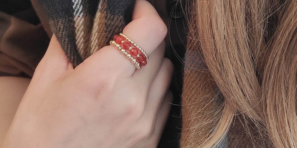 jesienny pierścionek elastyczny gold filled z czerwonym agatem AUTUMN oraz inne pierścionki założone na palec jesienny piękny pierścionek elastyczny z kuleczek gold filled i czerwonego agatu AUTUMN i pierścionki elastyczne z samych kuleczek gold filled założone na palec