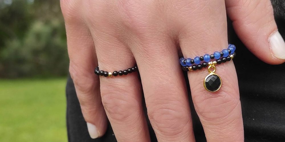 pierścionek eladtyczny z onyksem i jadeitem na ręce Złoty pierścionek elastyczny z kuleczką złota i czarnym onyksem i innymi pierścionkami elastycznymi założone na palcu