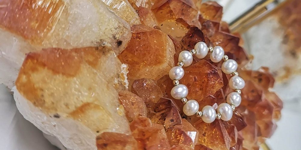 Damski stylowy i elegancki pierścionek elastyczny z naturalnych pereł i kuleczek gold filled położony na kryształach cytrynu